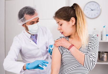 Young male doctor ready to make vaccination to teenage female visitor in hospitalの写真素材