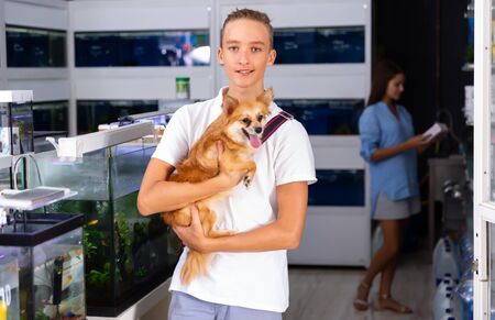 Young man with dog standing near aquarium in pet shopの写真素材