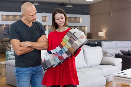 Female consultant helping man choosing upholstery fabric in furniture shop. Focus on both personsの写真素材