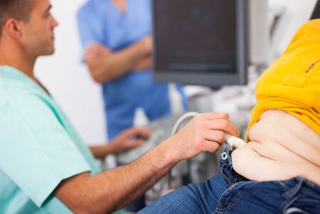 Man doctor examines a mature woman at abdomen with ultrasound, man on backgroundの写真素材