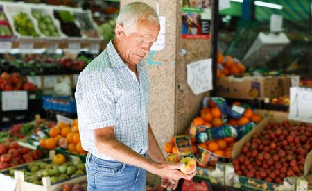 Happy elderly man looking for fresh organic fruits in local marketの写真素材