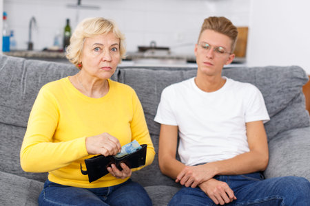 Mature woman giving pocket money her adult son at kitchen