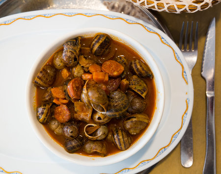 Top view of home style snails stewed with chorizo sausages in tomato sauce served in white bowl