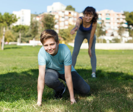 Happy family of mother and preteen son stretching together during training outdoors