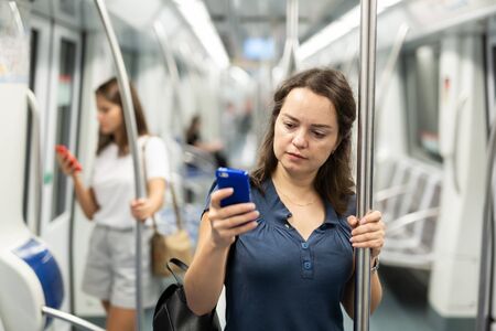 Positive woman reading from mobile phone screen in metroの写真素材