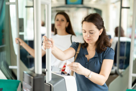 Young woman inserting ticket in modern punching machine, validating ticket in public transport