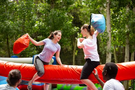Cheerful adult women having fun on inflatable pillow fight arena in outdoor amusement parkの写真素材