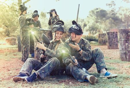 Portrait of male and female paintball players in camouflages with masks and marker guns prepared for gameの写真素材