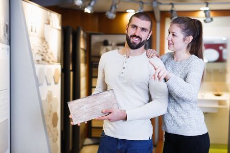 Positive young family standing with sample of kitchen ceramic tile in shopの写真素材