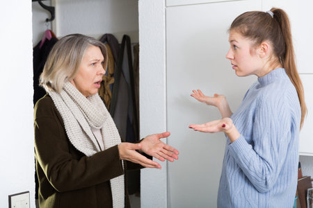 Two women young and mature talking emotionally in entrance hall of apartmentの写真素材