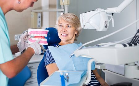 male dentist explaining future treatment to female patient on dental model in the dental clinicの写真素材