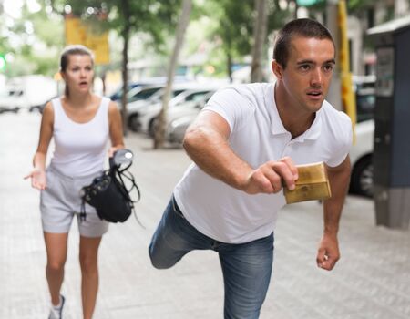 Male thief stealing purse from scared woman on streetの写真素材