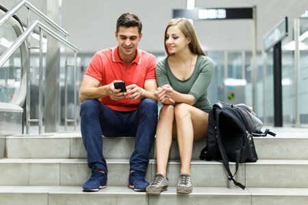 Couple is sitting on the stairs and looking on mobile in the metro.の写真素材