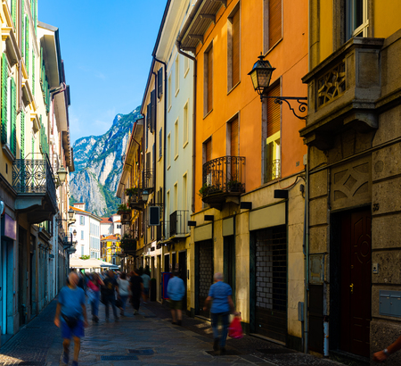 Typical busy narrow street of Italian city of Lecco on background of San Martino mountain in sunny summer day, Lombardyのeditorial素材