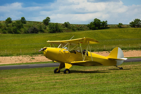 Yellow light biplane parked on green field on aerodrome