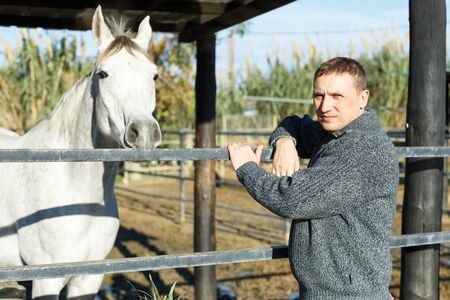 Portrait of cheerful man horse farm worker standing at stableの写真素材