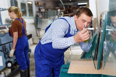 Portrait of confident man in blue overalls working in glass workshopの写真素材