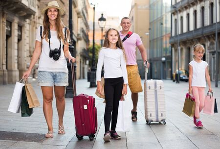 Happy germany traveling family of four strolling with luggage along European city streetの写真素材