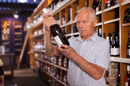 Older man looking for perfect wine for solemn occasion in wine storeの写真素材
