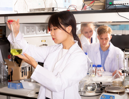 Adult Chinese female scientist holding flask of reagent at biochemical laboratory