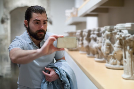 Adult male visitor using phone in sculptures exposition at museum