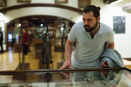 Attentive adult man exploring artworks in glass case in museum