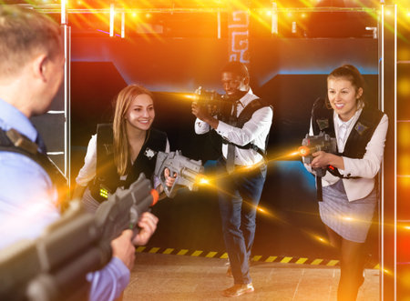smiling active men and women co-workers having corporate entertainment in laser tag room
