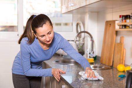 Portrait of positive brunette woman cleaning kitchen with ragの写真素材