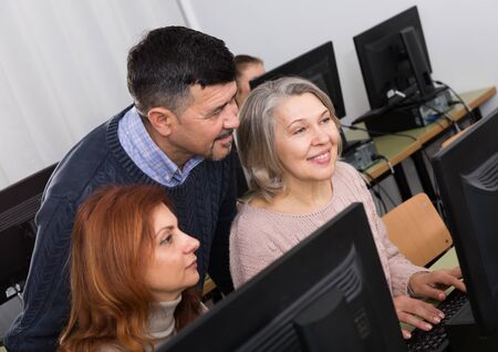 Friendly male teacher helping two smiling mature women to use computer in classroom

の写真素材