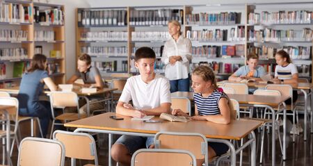 Schoolchildren preparing for lesson in the school library, reading and writingの写真素材