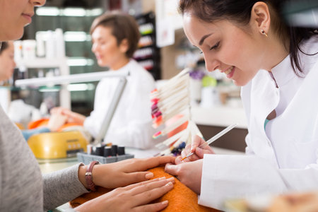 Manicurists giving manicure to female clients at nail salon