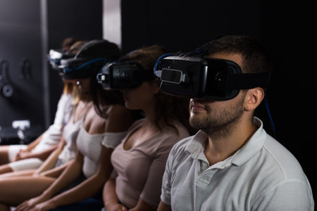 Young girls and guys wearing virtual reality goggles playing video games together indoors