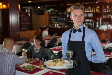 Portrait of smiling waiter with serving tray meeting restaurant guestsの写真素材