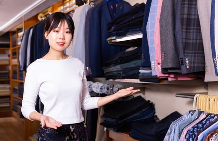 Adult Chinese salesgirl offering stylish suit coats in men clothing storeの写真素材