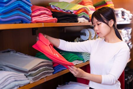 Nice Chinese girl choosing stylish mens polo shirt in clothing storeの写真素材