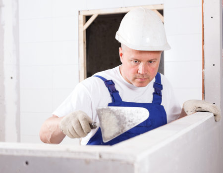 Construction worker with wall plastering tools mudding plaster wall in repairable room