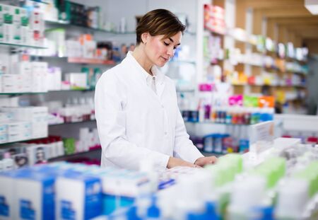 Positive female pharmacist arranging assortment of products in pharmacyの写真素材
