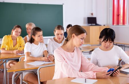 Group of focused female students using phones in common research at class in auditoriumの写真素材