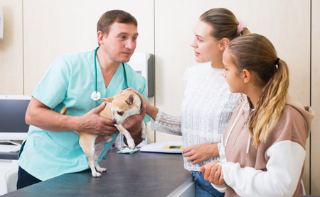 Troubled woman and preteen girl with little dog asking for professional advice from veterinarian