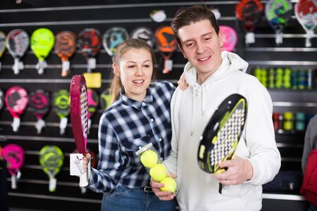 Positive couple are choosing padel racket and balls in the sportive storeの写真素材
