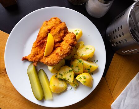 Top view of fried chicken cutlet breaded with Parmesan served with boiled potatoes, greens and pickles. Traditional Czech dishの写真素材