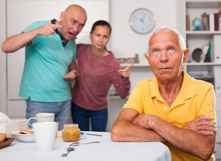 Upset senior man sitting at table, family couple quarrelling on backgroudの写真素材