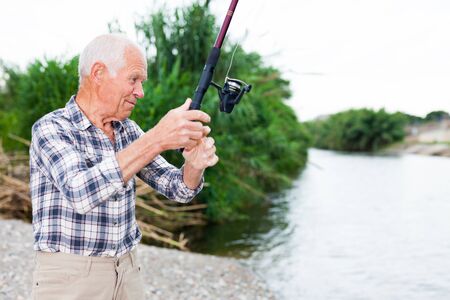 Positive adult man with rod relaxing and enjoying fishing by lakesideの写真素材