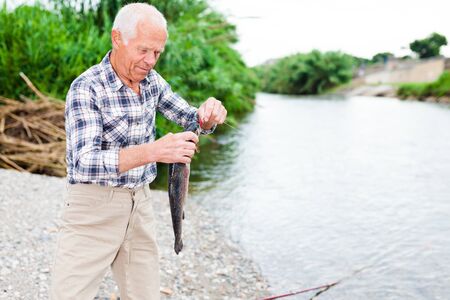 Happy adult man enjoying fishing and removing catch from hookの写真素材