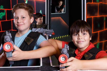 Portrait of two glad teen boys standing with laser guns ready for lasertag game indoorsの写真素材