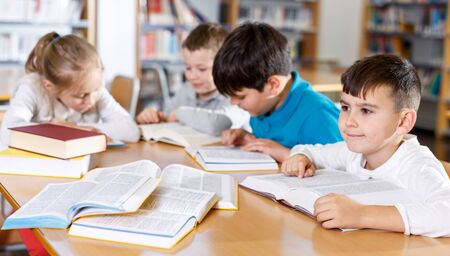 Group of intelligent children studying together in school library, reading booksの写真素材