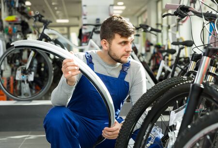 Cheerful professional man holding cycle frame in bicycle shopの写真素材