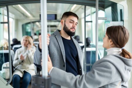 Attractive girl and bearded guy talking in city bus on way to work in fall dayの写真素材