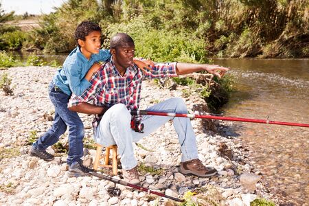 Portrait of fishermen - African boy and his father fishing with rods on riverの写真素材
