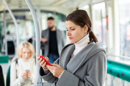 Positive woman reading from mobile phone screen in tram